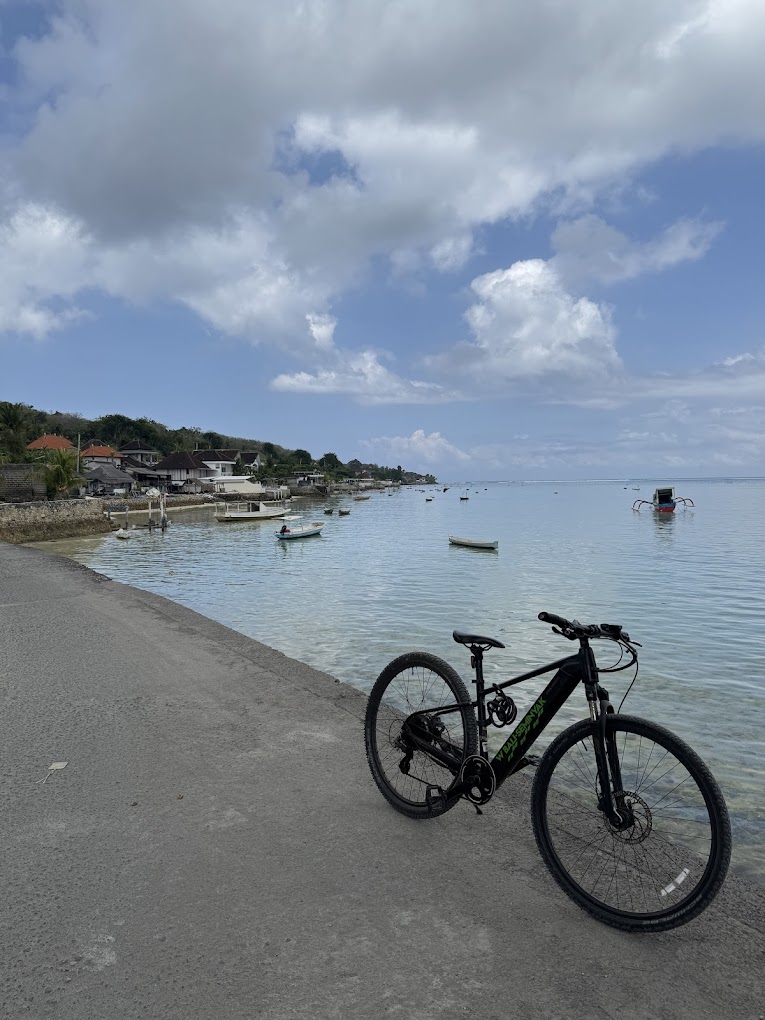 UNIKAT e-bike on scenic coastal road with traditional boats and harbor on Nusa Lembongan