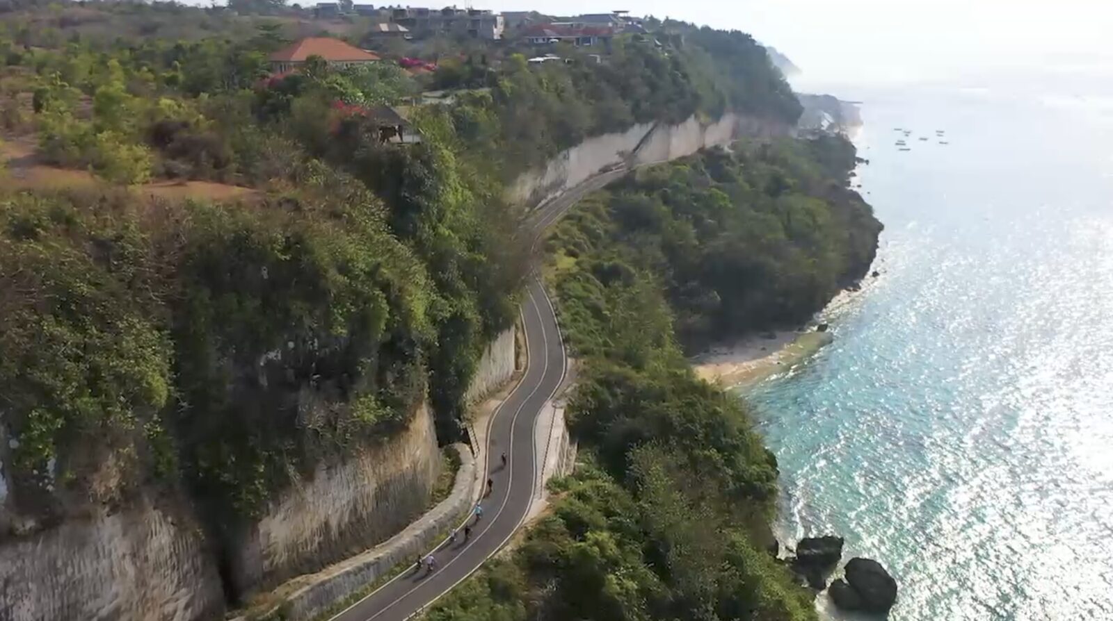Cyclists riding e-bikes along a dramatic Bali coastal cliff road above turquoise ocean — UNIKAT E-Bike Tours
